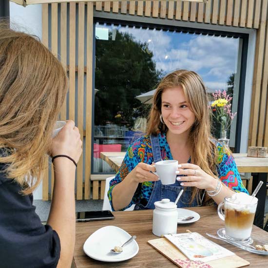 Dvě mladé ženy povídající si u kávy na zahrádce před Mandlárnou